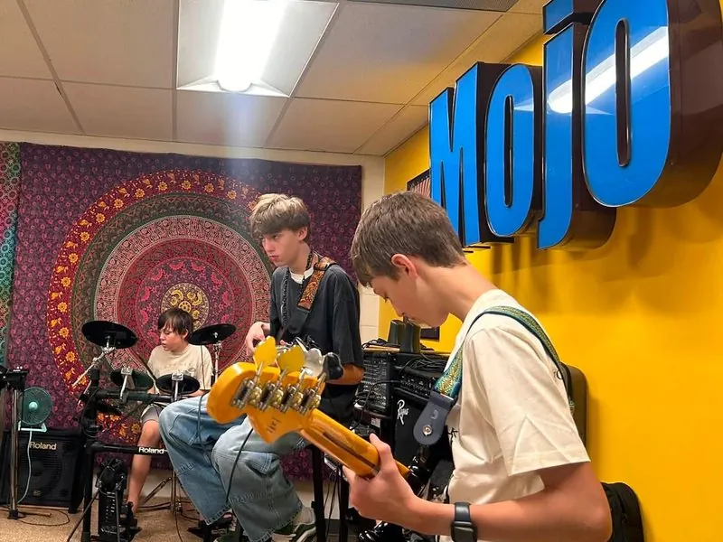 Teen students playing bass, guitar, and drums together in the Mojo's Music Academy band room