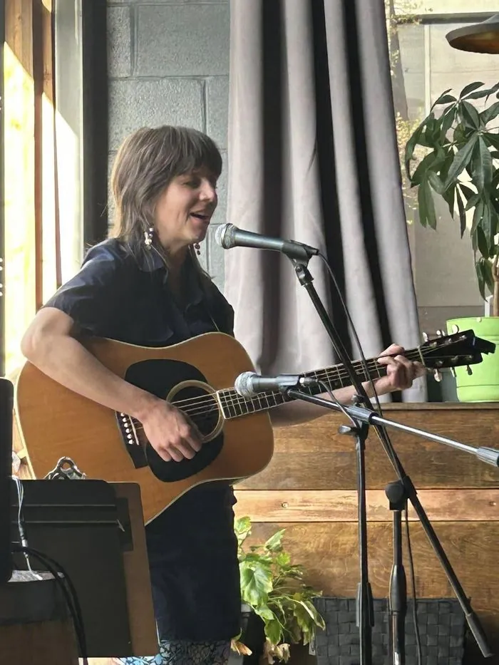 Adult student singing and playing acoustic guitar at an open mic