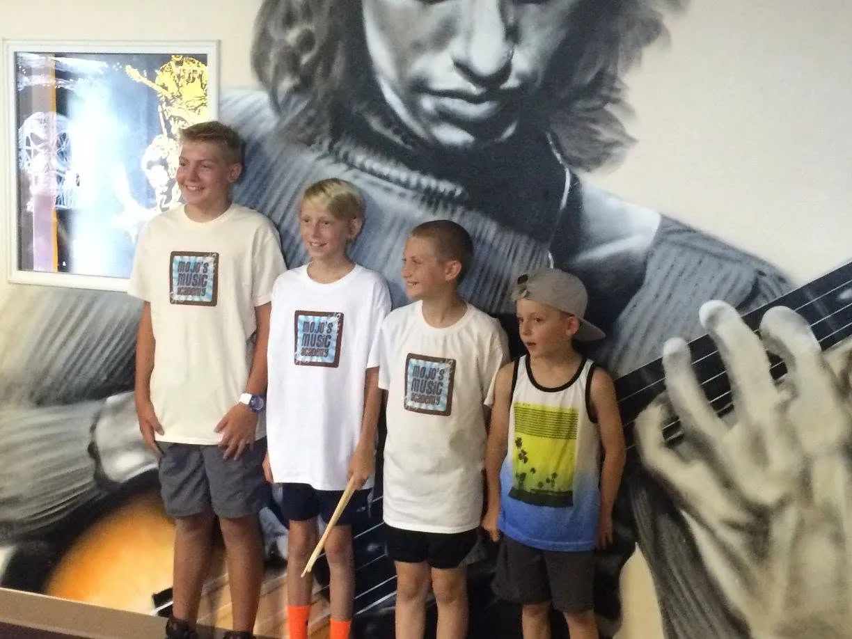 Group of Mojo's Music Academy summer camp students posing in front of the studio mural