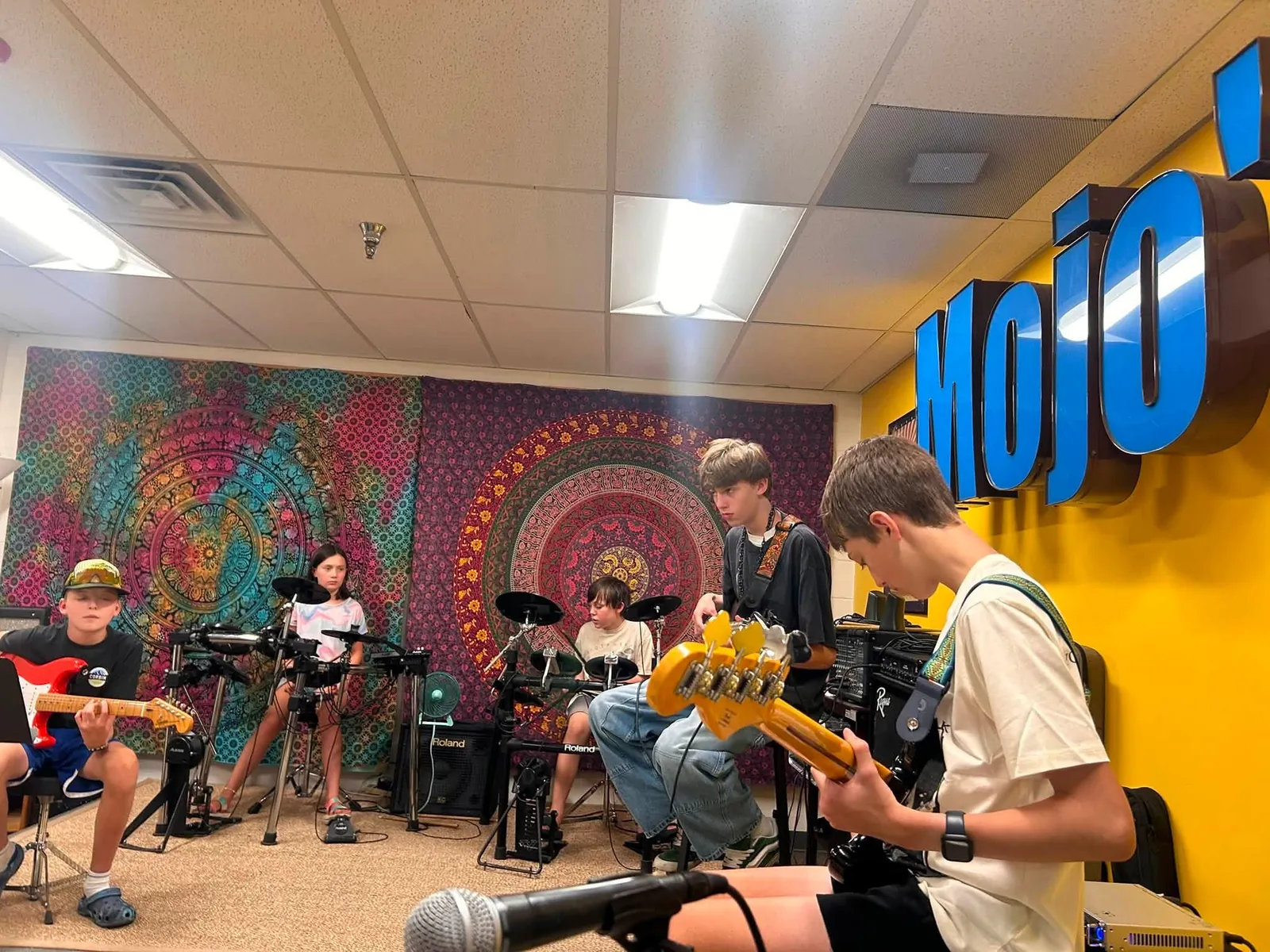 Teen students playing bass, guitar, and drums together in the Mojo's Music Academy band room