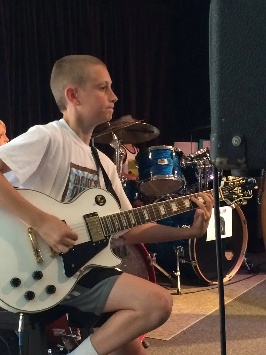 Student playing electric guitar on stage at Mojo's Music Academy