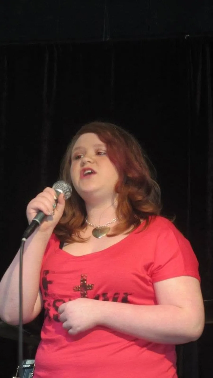 Student singing into a microphone on stage at Mojo's Music Academy